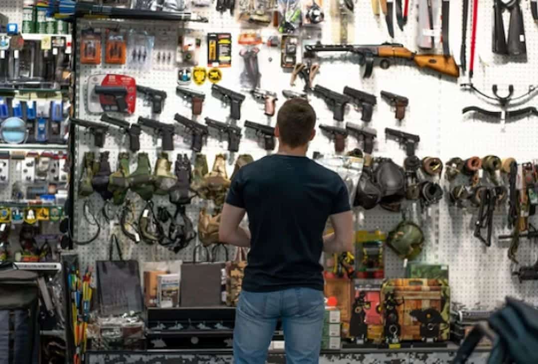 a person looking at the guns on the wall in a gun shop