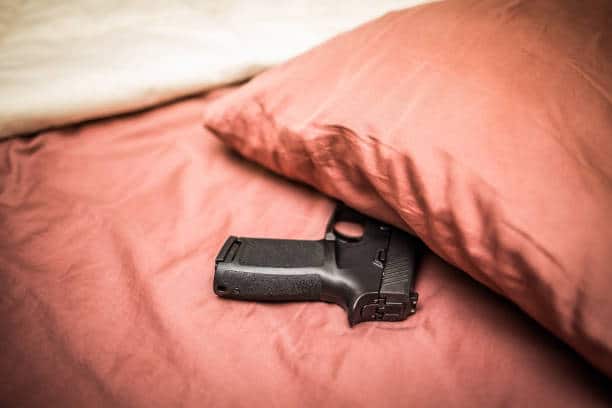 Gun on a bed below a pillow